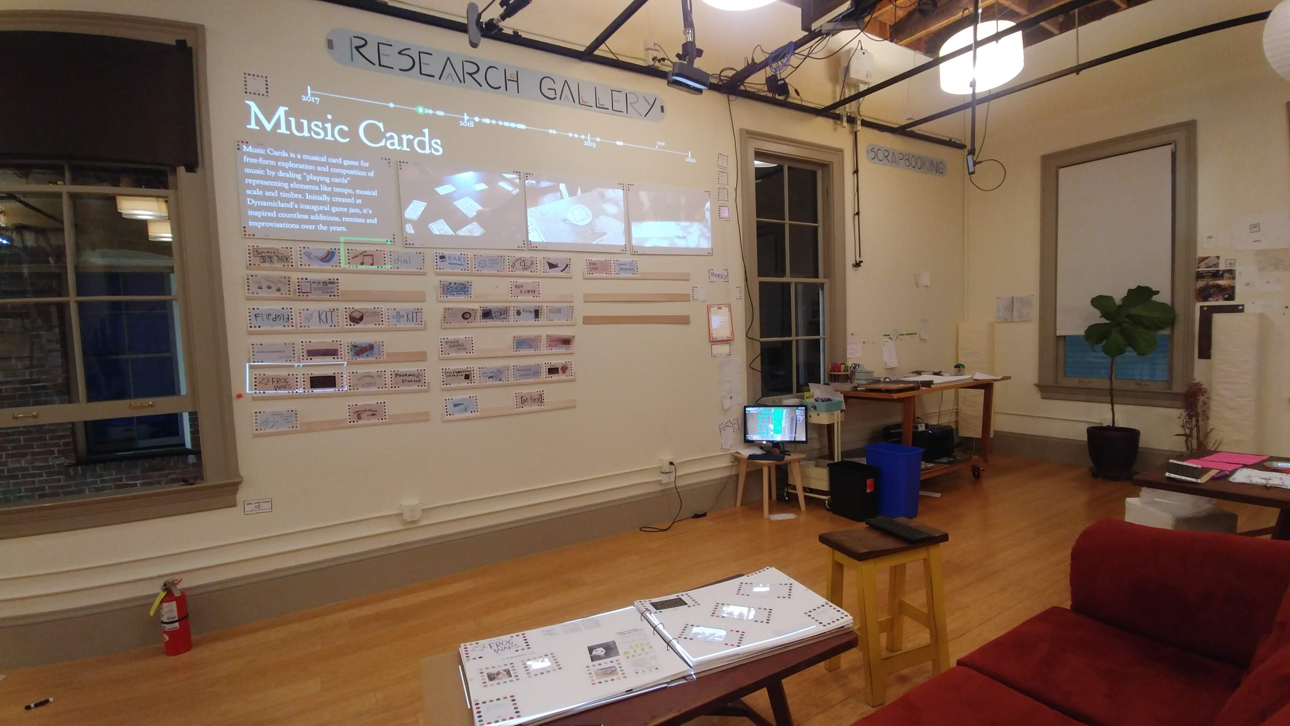 The Research Gallery space, with couch, coffee table and scrapbook, card wall, theater screens and scrapbooking table